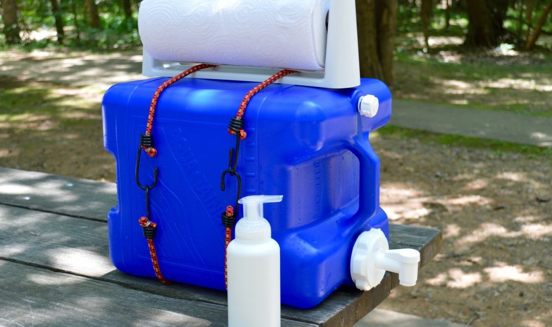 DIY Camping Handwashing Station with blue water jug, soap bottle, and paper towels on a picnic table