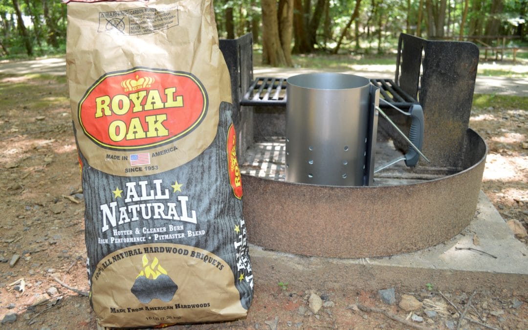 a bag of charcoal beside a chimney starter in a campground fire pit