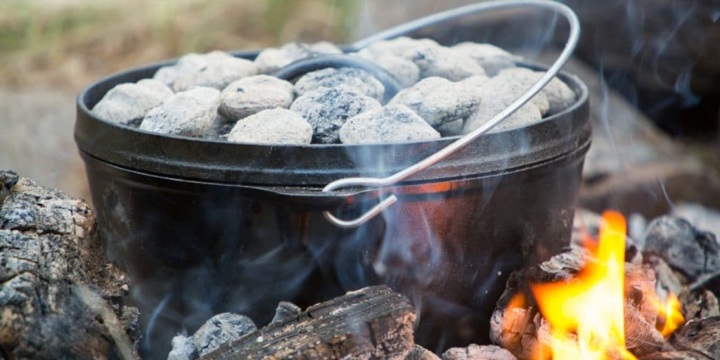 Dutch oven with charcoal briquettes on top in a campfire