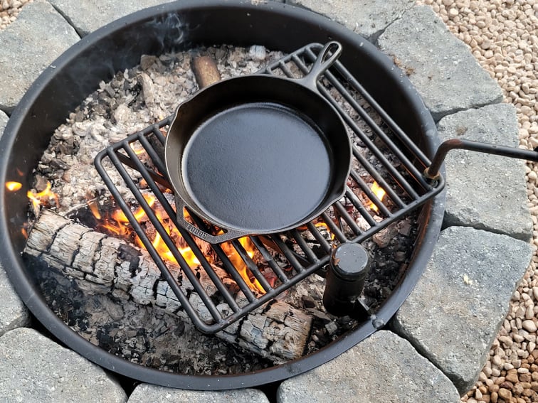 A clean, seasoned cast iron skillet sitting on a campfire grate