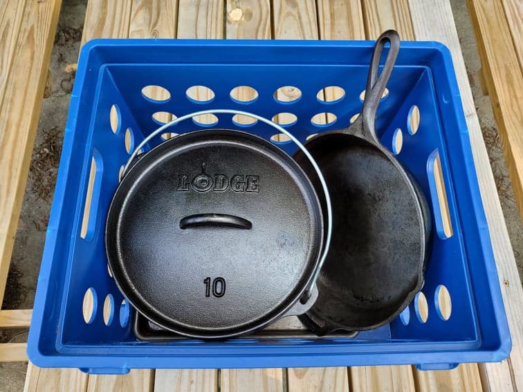 Dutch oven and cast iron skillet in a blue crate used to pack cast iron cookware for camping