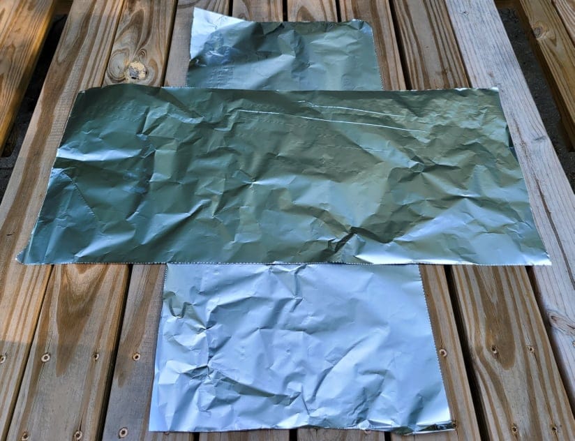two aluminum foil pieces on a picnic table prepared for foil packet cooking 