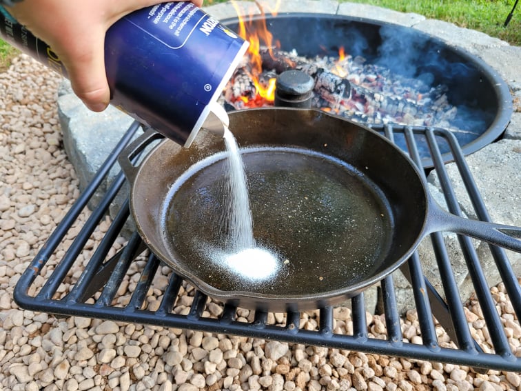 Pouring scrubbing salt into a dirty cast iron skillet 