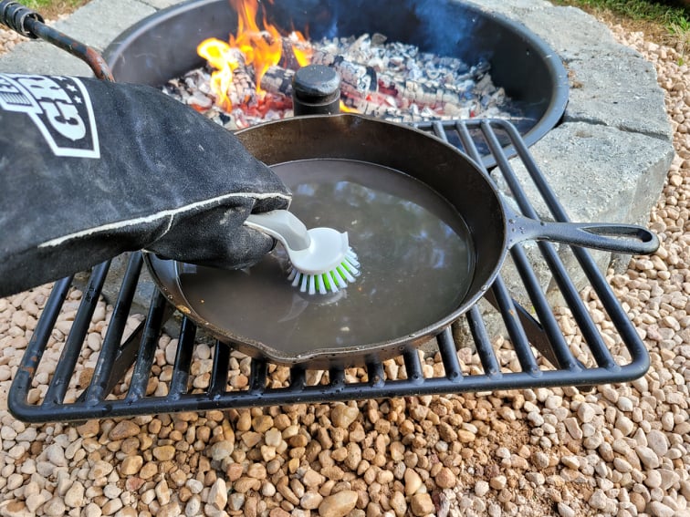 Scrubbing a warm cast iron skillet with a heat-resistant glove and nylon dish brush