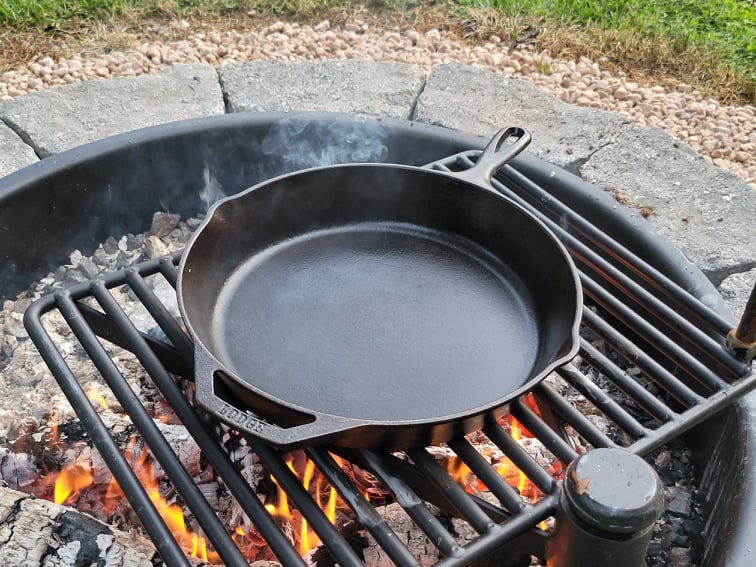 Heating oiled cast iron skillet over a campfire until smoking to season it