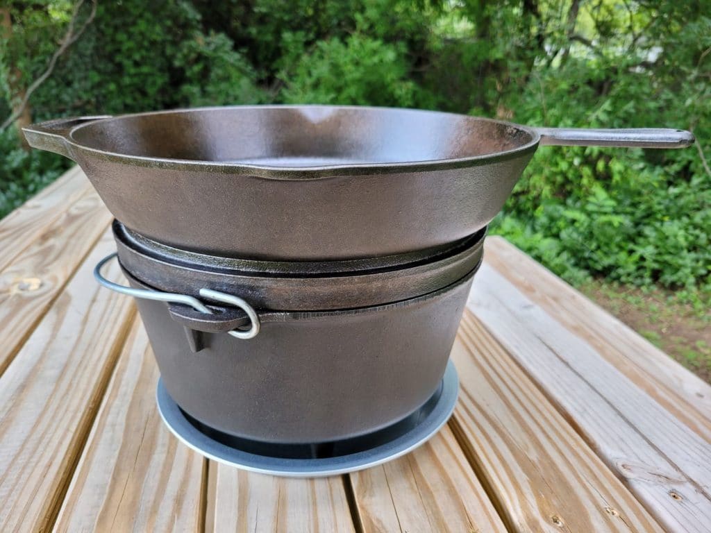 Cast iron dutch oven sitting on a metal pie plate with a skillet stacked on top