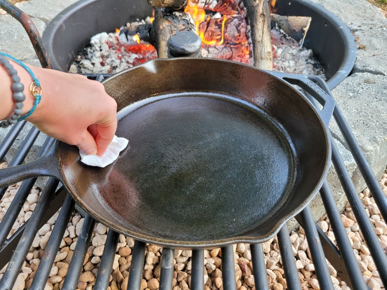Wiping a very thin layer of oil on the cast iron skillet to prepare for seasoning