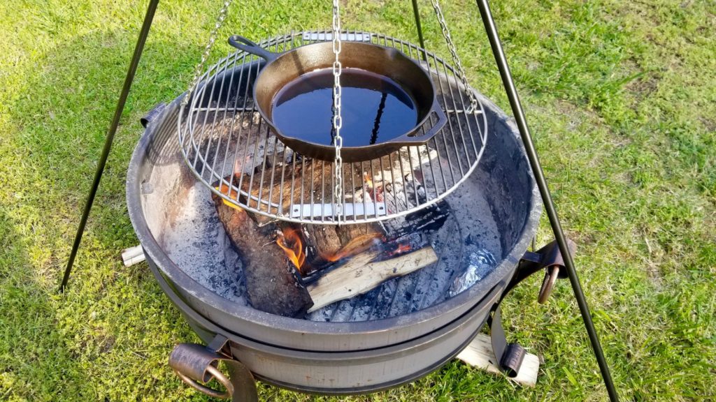 cast iron skillet on a grill rack suspended from a tripod over the fire