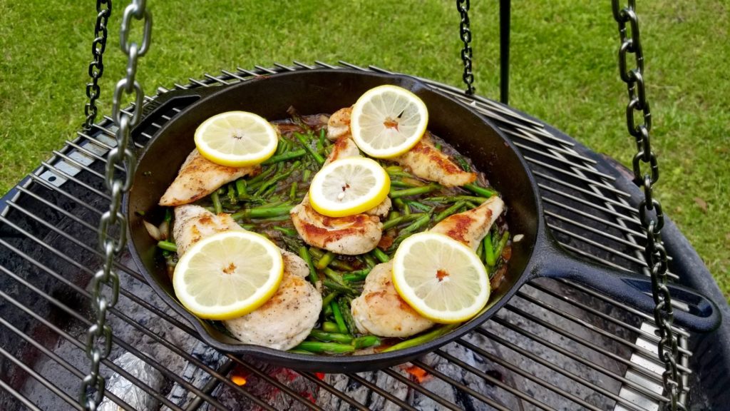 asparagus with browned chicken breasts topped with lemon slices in a cast iron skillet 