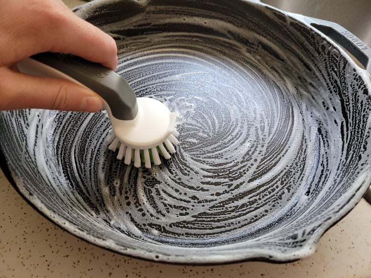cleaning a cast iron pan with soap and a nylon bristle brush