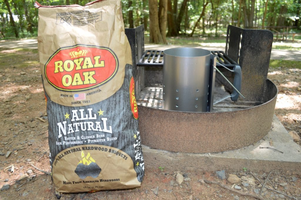 a bag of charcoal sitting beside a charcoal chimney starter in a steel fire ring 