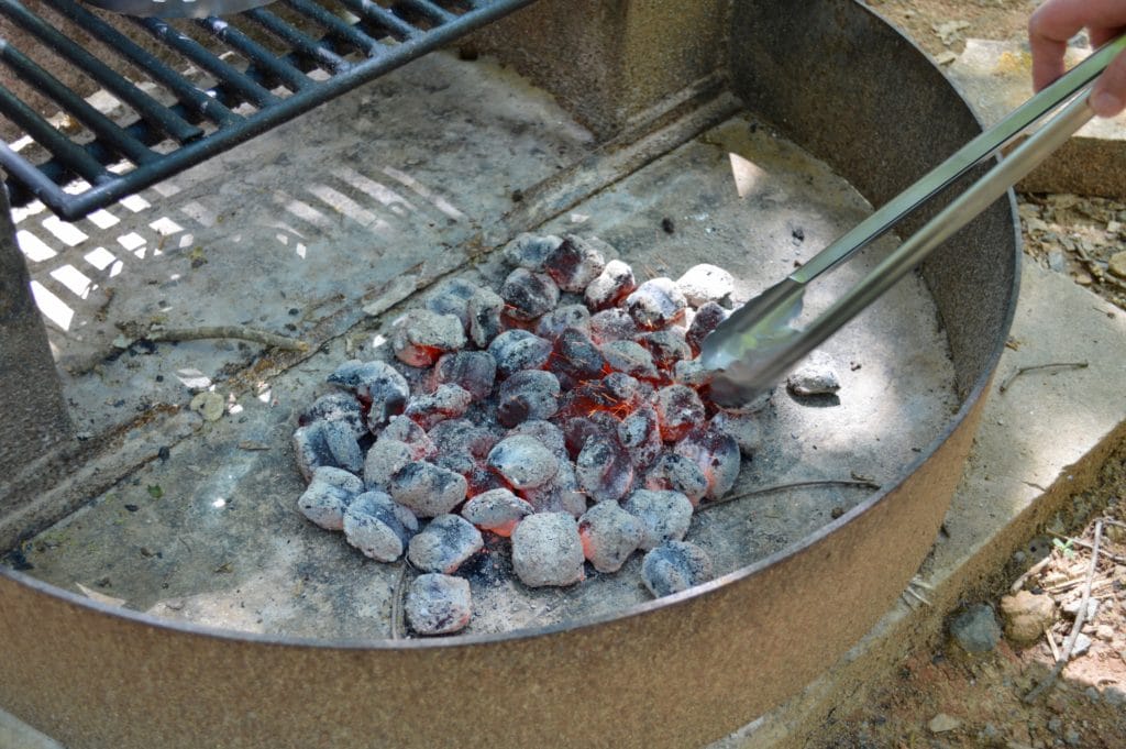 arranging hot charcoal in the fire pit with long-handled tongs