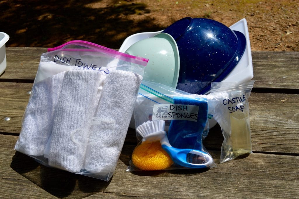 clean dishes in a dry dishpan with ziplock bags containing soap, sponges, and towels to wash dishes while camping
