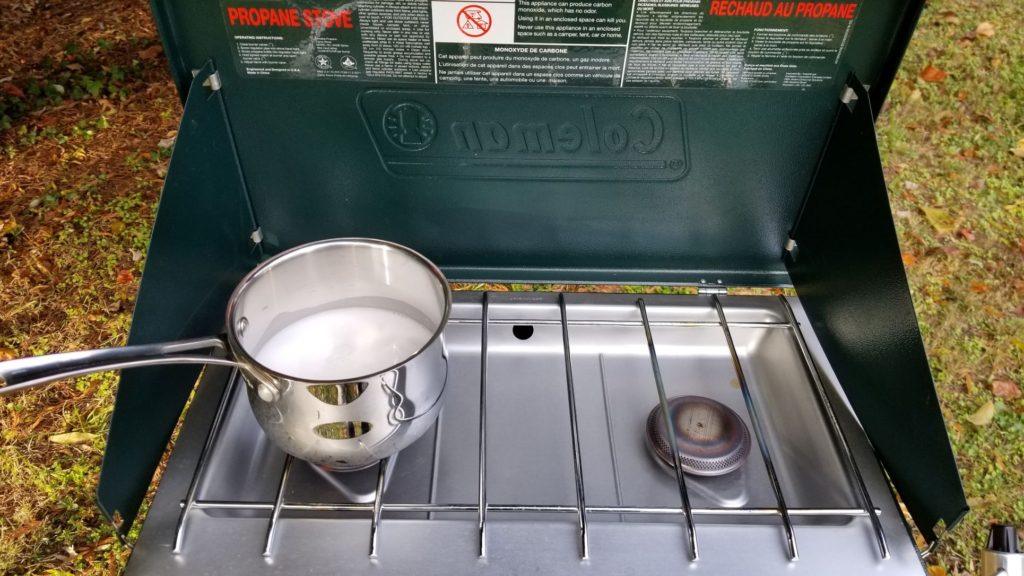 saucepan filled with coconut milk heating on a propane camping stove