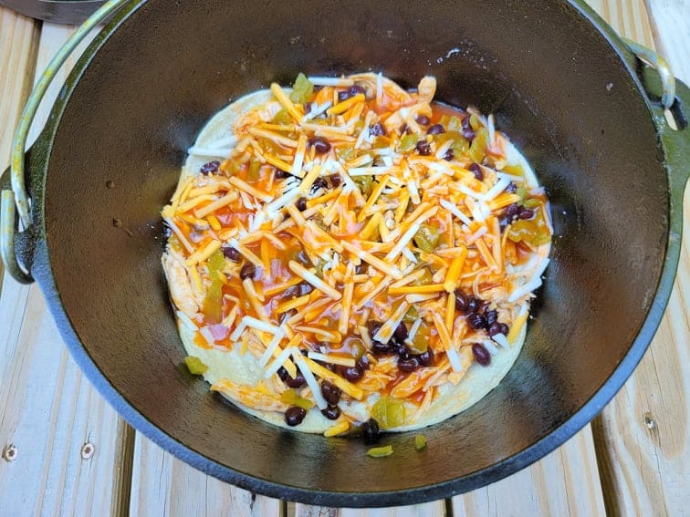 Layered tortillas, chicken, green chiles, beans, cheese, and enchilada sauce in dutch oven 