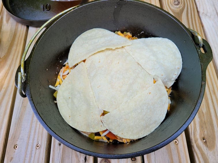 Layered tortilla halves on top of enchilada filling in dutch oven 