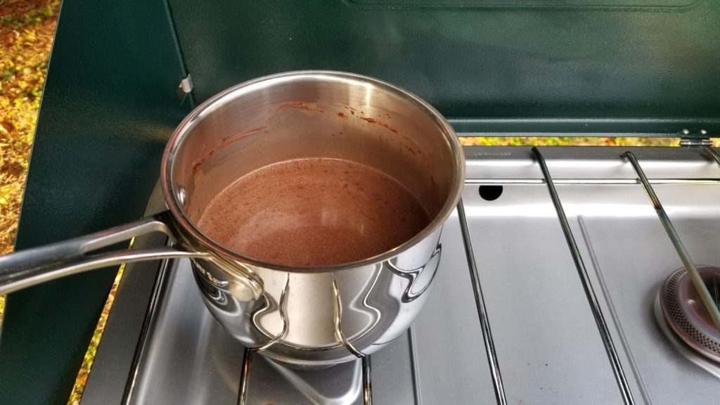 paleo hot chocolate heated in a silver pan over a propane camping stove