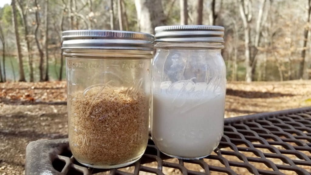 pre-made dry paleo instant oatmeal mix in a mason jar sitting beside a jar of almond milk on a picnic table