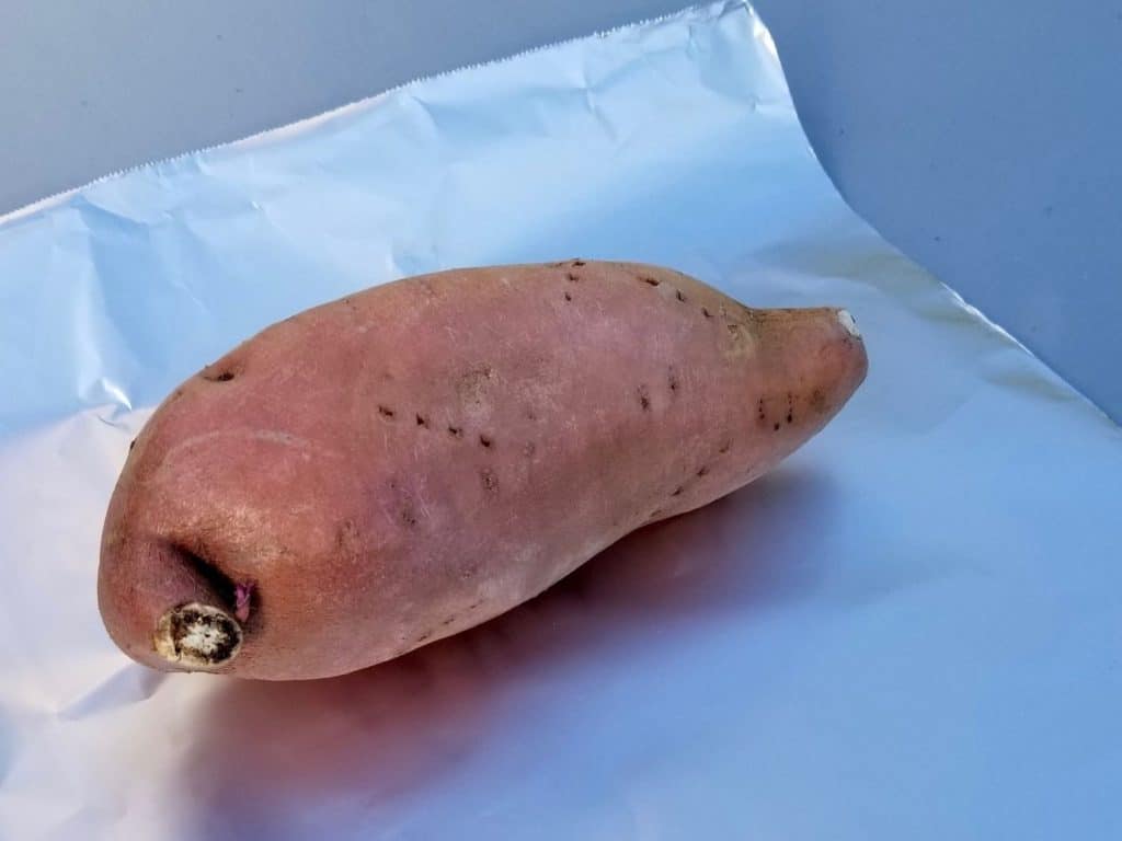 wrapping a sweet potato in foil to prepare it for cooking 