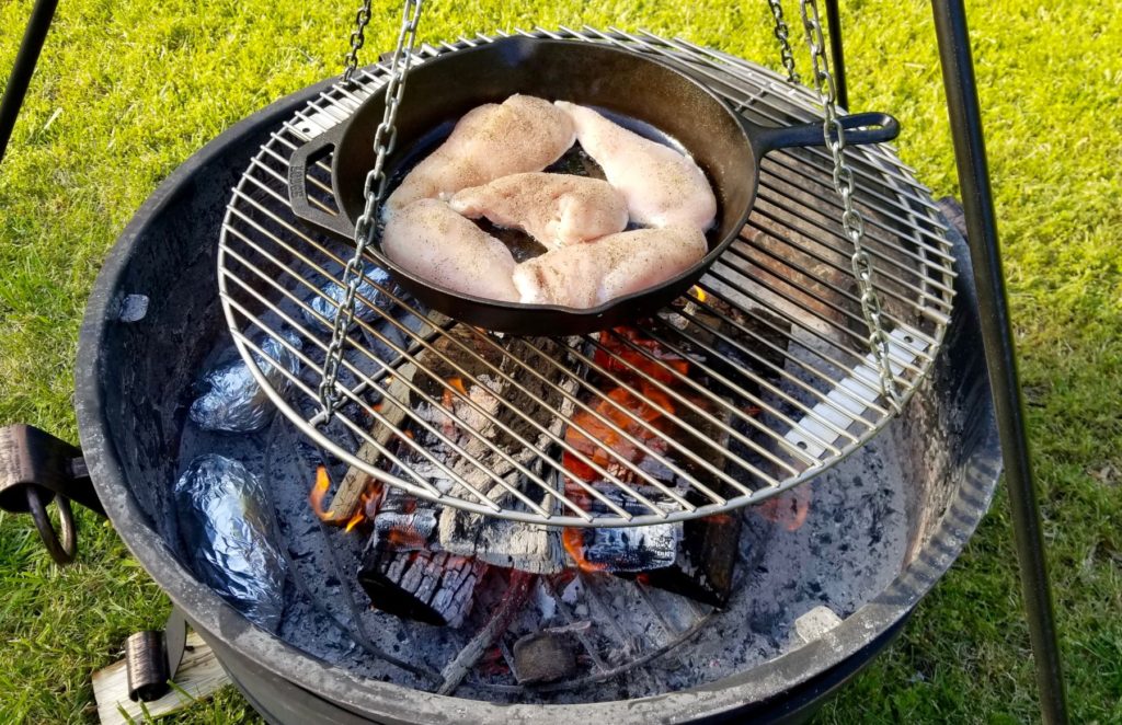 seasoned chicken breasts cooking in a cast iron skillet over the fire pit 