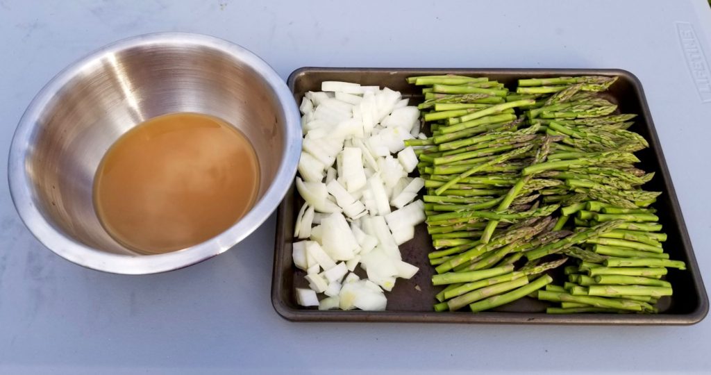a bowl of lemon honey marinade sauce next to a tray of chopped onion and asparagus 