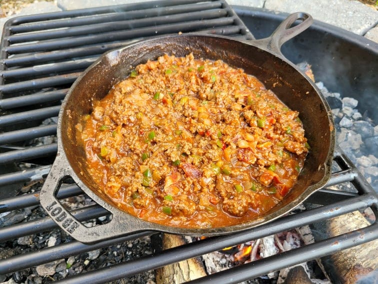 Campfire Sloppy Joe mix in a cast iron skillet simmering over the fire