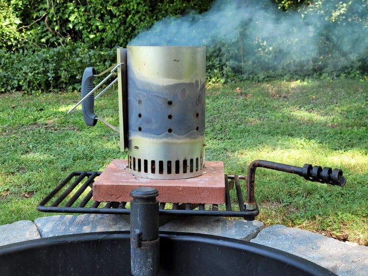 a smoking charcoal chimney starter on a fire pit grate