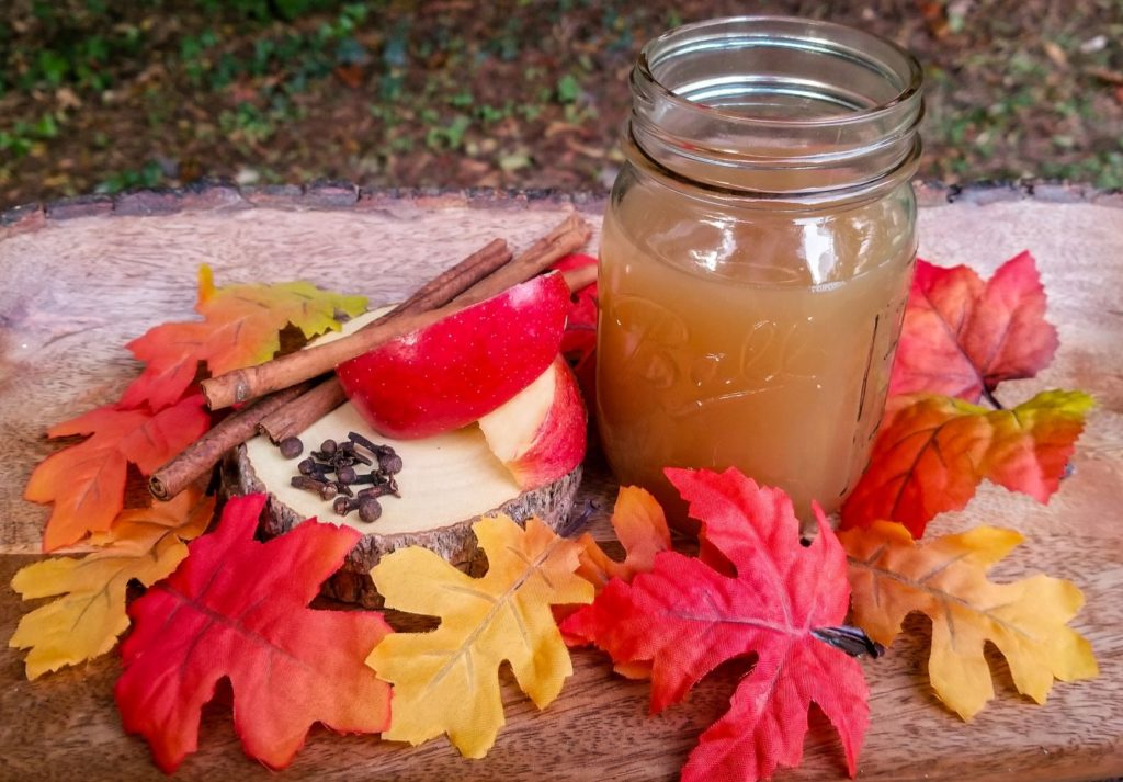 Spiced apple cider in a glass mason jar surrounded by fall leaves