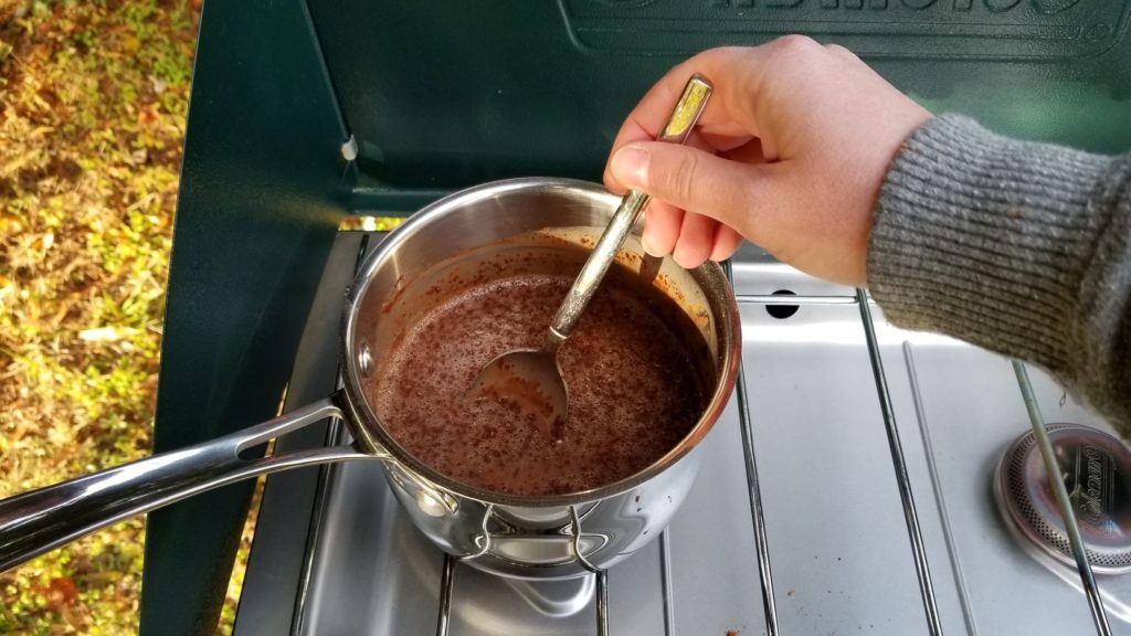 paleo hot chocolate ingredients combined in a silver saucepan on a propane camping stove