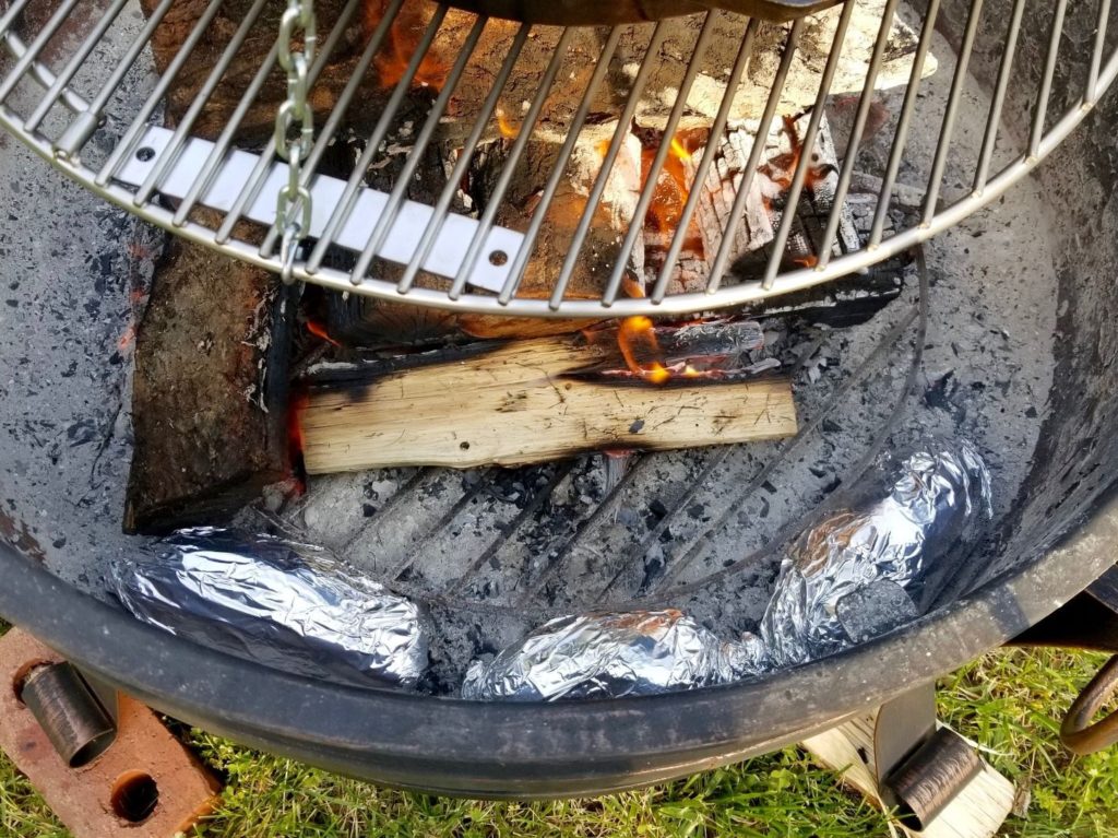 Three sweet potatoes wrapped in aluminum foil cooking in a fire pit 