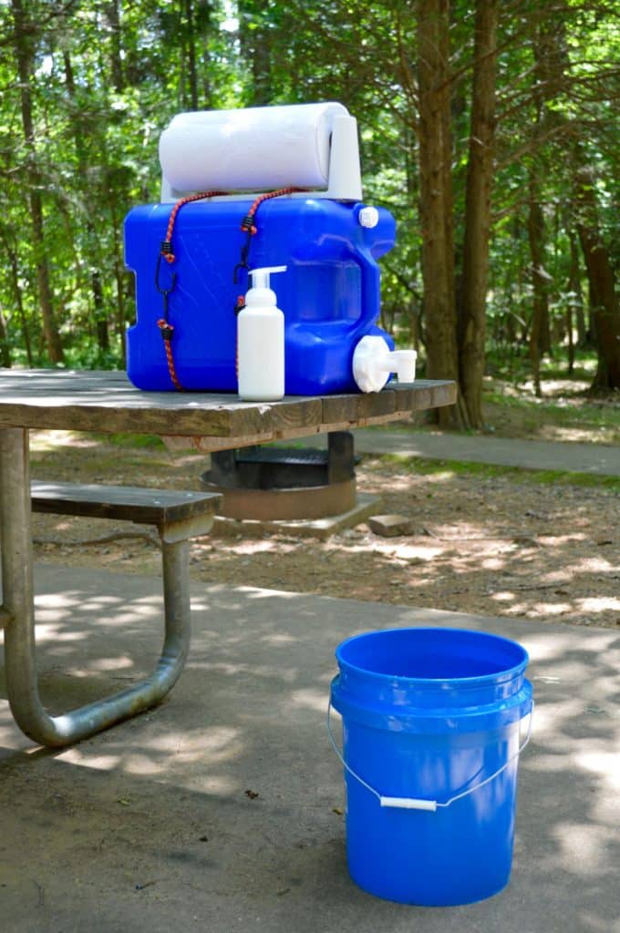 Camping handwashing station set up on the edge of a picnic table with a blue bucket underneath to catch runoff