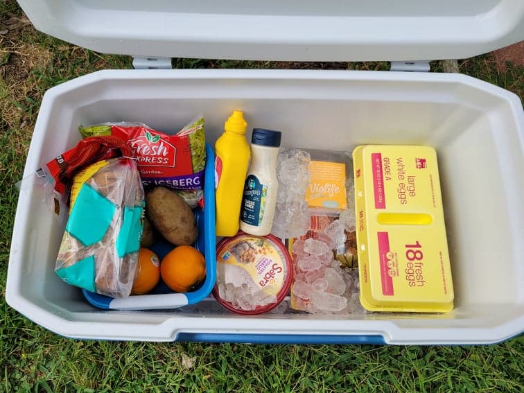 cooler with ice, meat, a produce bin, eggs, bread, and condiments  