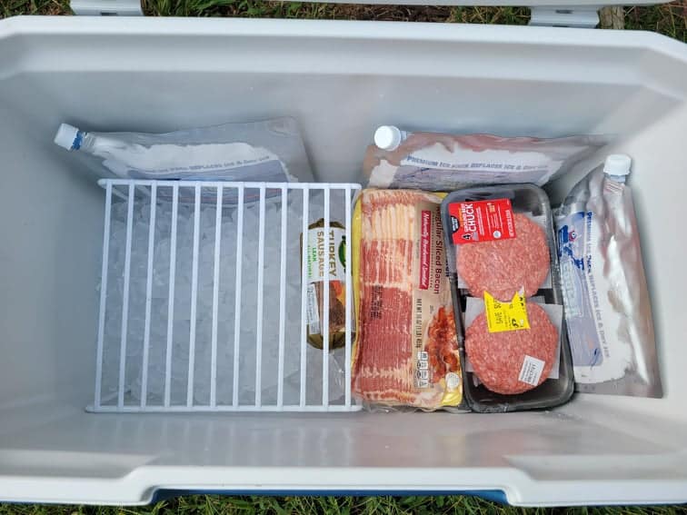 cooler with ice in the bottom, a wire rack above, and packaged meat placed on the ice