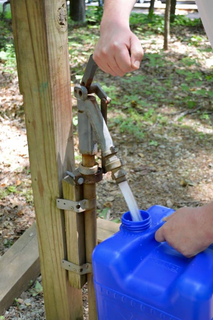 water from a faucet filling a large, blue, plastic water jug at a campground 