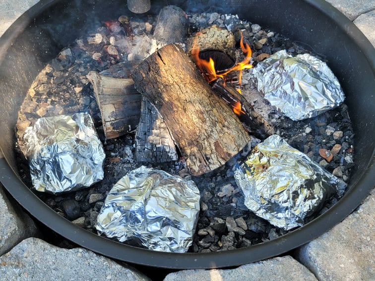chicken, bacon, and ranch foil packets cooking in a fire pit