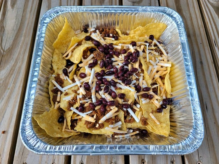 Tortilla chips, taco meat, black beans, and shredded cheese in a foil pan to make camping nachos