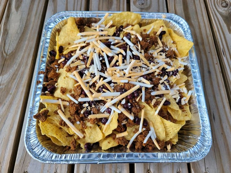 Layered tortilla chips and nacho ingredients in a foil pan ready to cook 