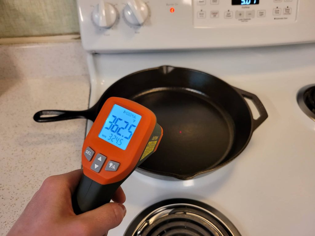 Using an infrared laser thermometer to check the temperature of the inside bottom of a cast iron skillet on a stovetop burner 