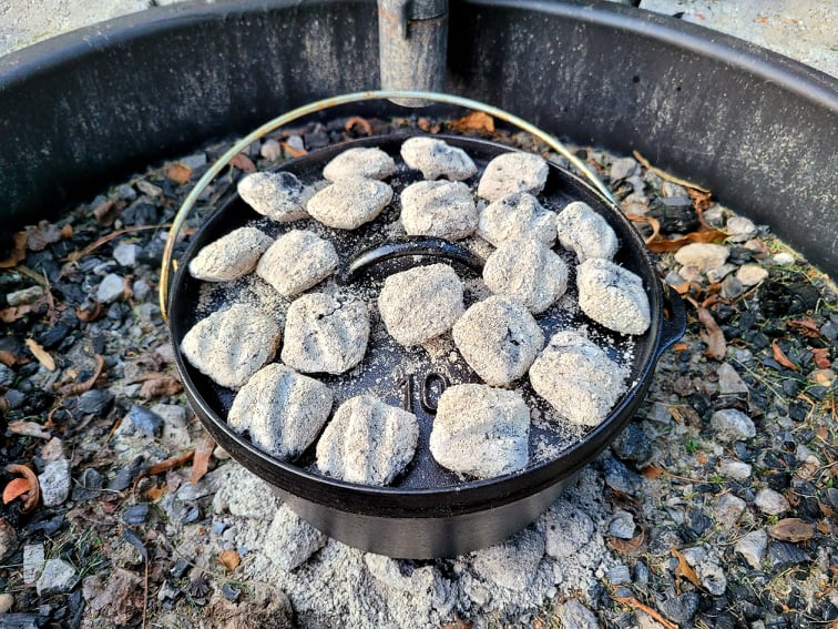 dutch oven in a fire pit with charcoal briquettes on top and underneath the pot