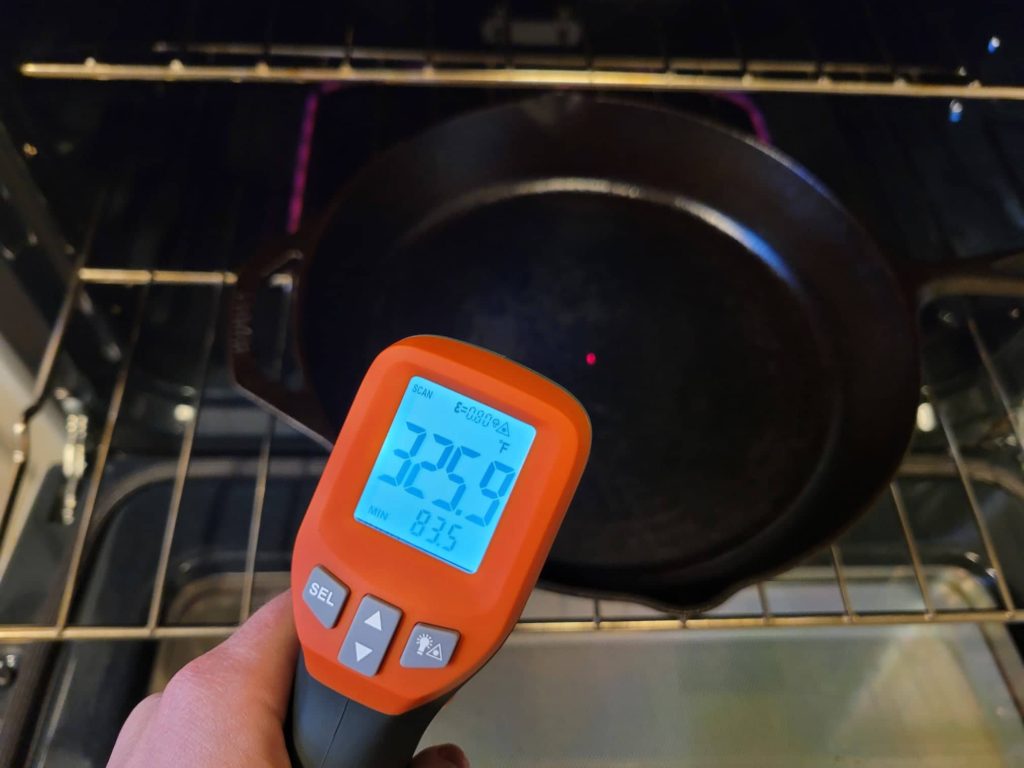 Using an infrared laser thermometer to check the temperature of the inside bottom of a cast iron skillet in the oven.