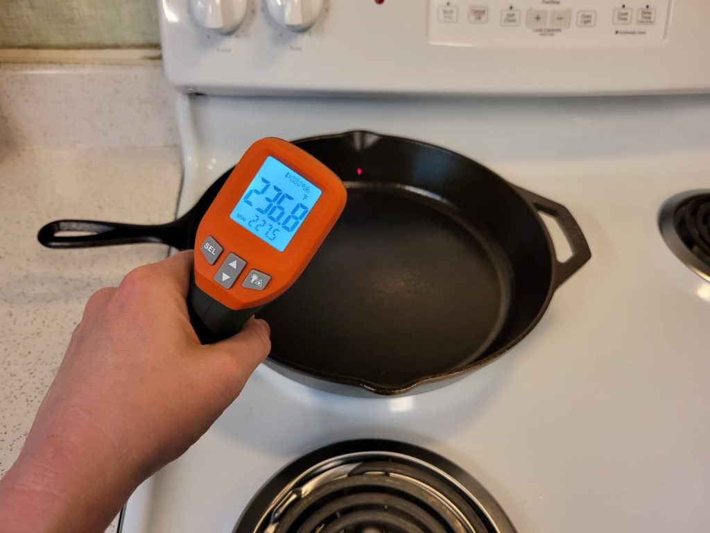 Using an infrared laser thermometer to check the temperature of the inside sidewalls of a cast iron skillet on a stovetop burner 