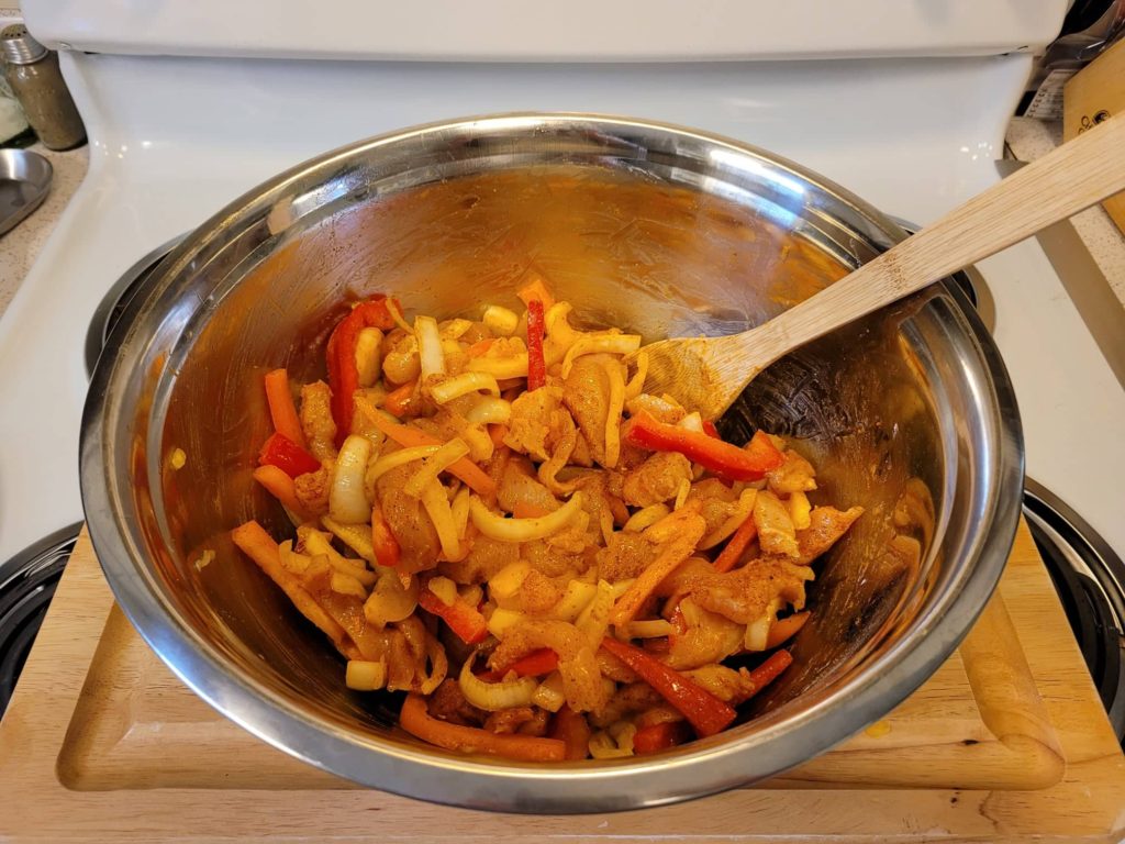 chicken and fajita veggie strips with seasoning in a large mixing bowl