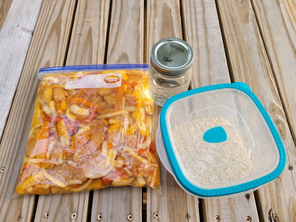 Pre-prepared fajita chicken, veggies, and rice in containers on a picnic table