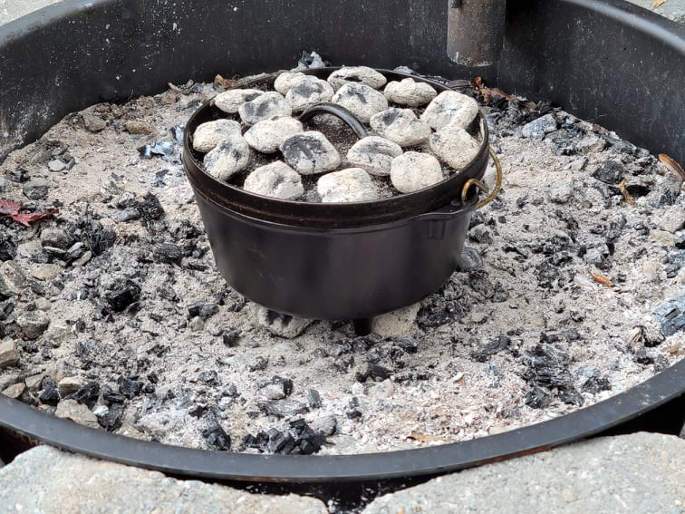 Dutch oven with charcoal underneath and on top in a fire pit