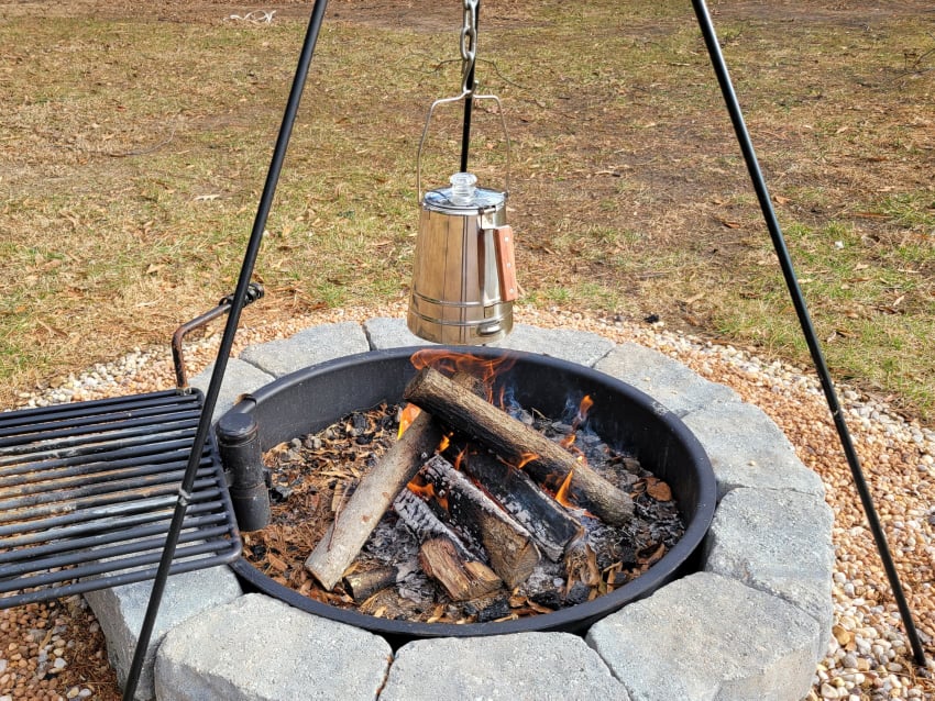 coffee percolator hanging on a camping tripod over a fire pit
