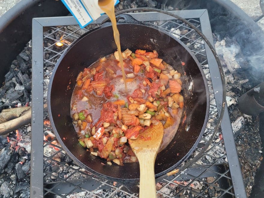 adding beef stock to the dutch oven with the stew veggies