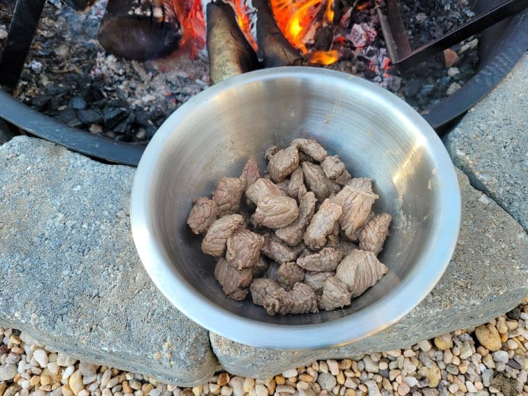 cooked stew beef in a silver bowl by the fire pit