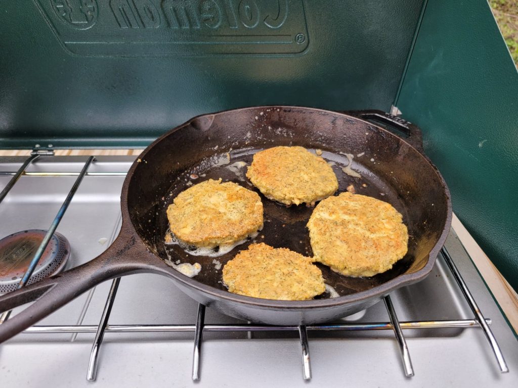 cooking camping stove salmon patties in a cast iron skillet