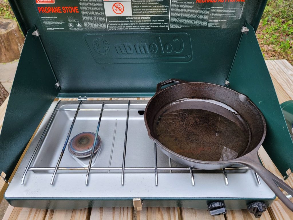 preheating cooking oil in a cast iron skillet on a camping stove