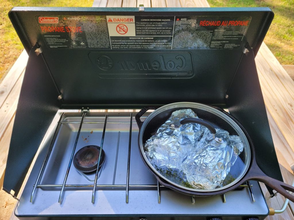 Cooking foil packet meals on camp stove in a skillet with lid